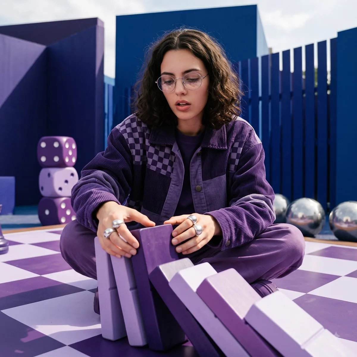Person in glasses tipping a row of giant purple dominoes